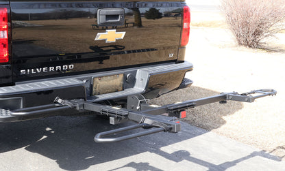 Angled view of the Sunlite HRT-100 Trike Auto Rack for 2-inch Receivers mounted on the hitch on a black pickup truck in an outdoor setting.