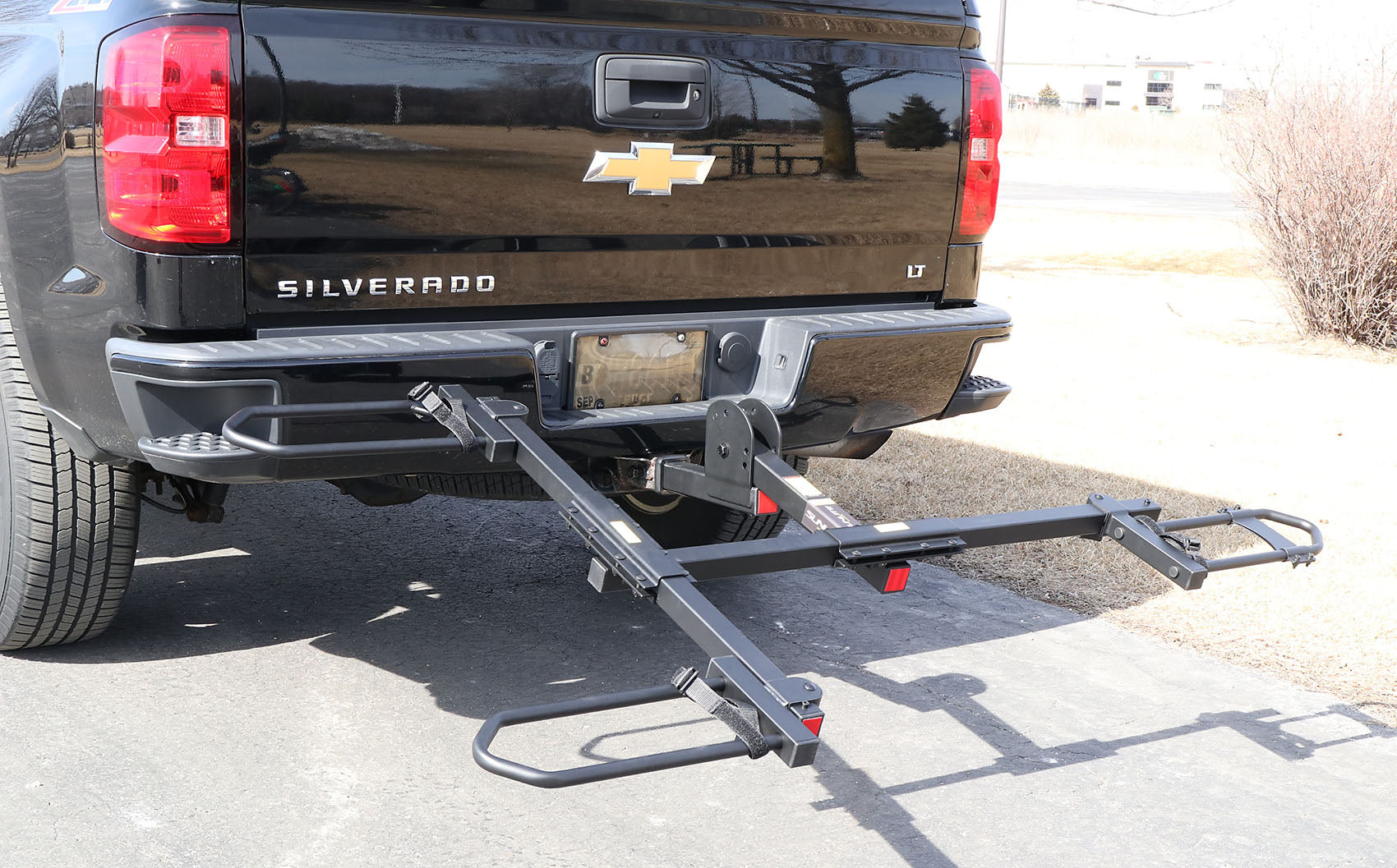 Tilted down view of the Sunlite HRT-100 Trike Auto Rack for 2-inch Receivers mounted on the hitch on a black pickup truck in an outdoor setting.