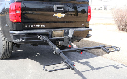 Tilted down view of the Sunlite HRT-100 Trike Auto Rack for 2-inch Receivers mounted on the hitch on a black pickup truck in an outdoor setting.
