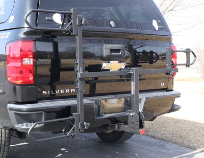 Folded up angled view of the Sunlite HRT-100 Trike Auto Rack for 2-inch Receivers mounted on the hitch on a black pickup truck in an outdoor setting.