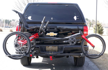Rear view of the Sunlite HRT-100 Trike Auto Rack for 2-inch Receivers mounted on the hitch on a pickup truck  with a red Hase Trigo on the rack in an outdoor setting.