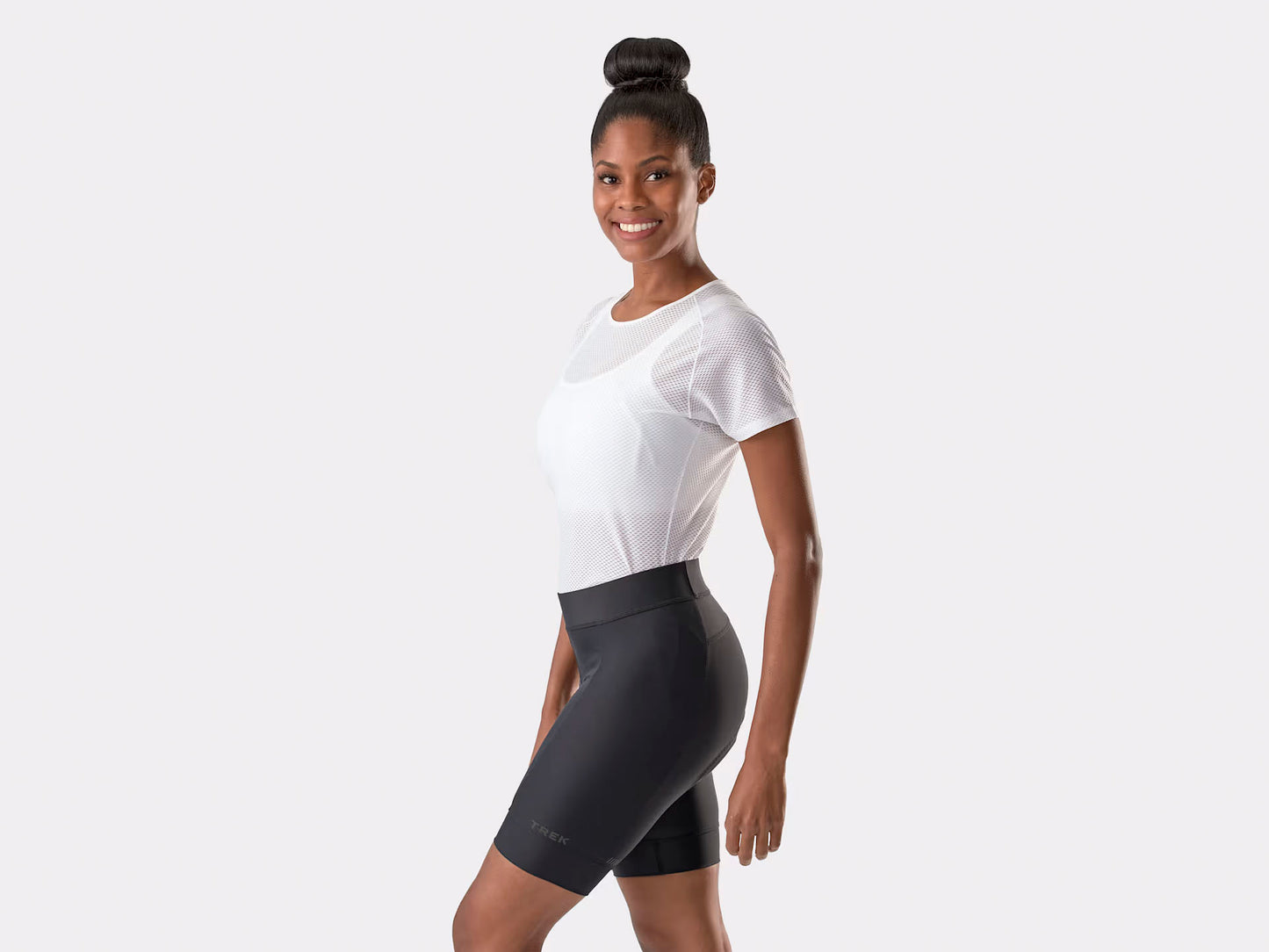 Studio side view of a woman wearing black fitted cycling shorts that extend about three inches above her knees with a small Trek logo approximately two inches above the bottom of the left leg of the shorts. 