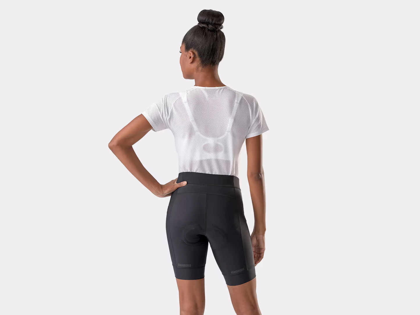 Studio back view of a woman wearing fitted black cycling shorts with small reflective dash details about two inches above the bottom of each leg of the shorts. 