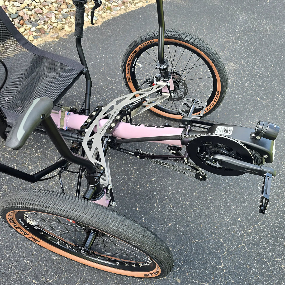 Closeup view of the front suspension, grab handle, Shimano motor, headlight  and quick adjust on the Azub Demo Ti-Fly 20 Enviolo Shimano EP6 Pastel Violet Recumbent Trike in an outdoor setting.
