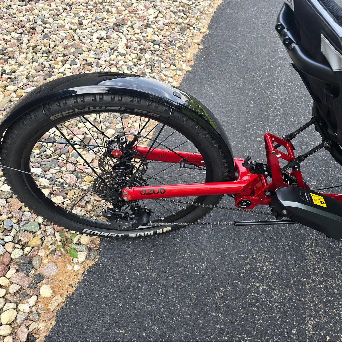 Closeup view of the rear wheel, rear fender, cassette, rear derailleur and Shimano battery on the Azub Demo Ti-Fly X Shimano EP6 Ruby Red Recumbent Trike in an outdoor setting.