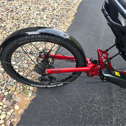 Closeup view of the rear wheel, rear fender, cassette, rear derailleur and Shimano battery on the Azub Demo Ti-Fly X Shimano EP6 Ruby Red Recumbent Trike in an outdoor setting.