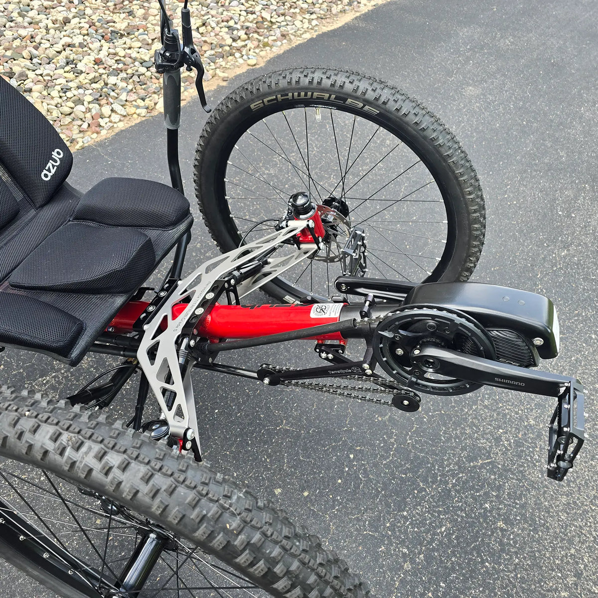 Closeup view of the front suspension, quick adjust and Shimano motor on the Azub Demo Ti-Fly X Shimano EP6 Ruby Red Recumbent Trike in an outdoor setting.