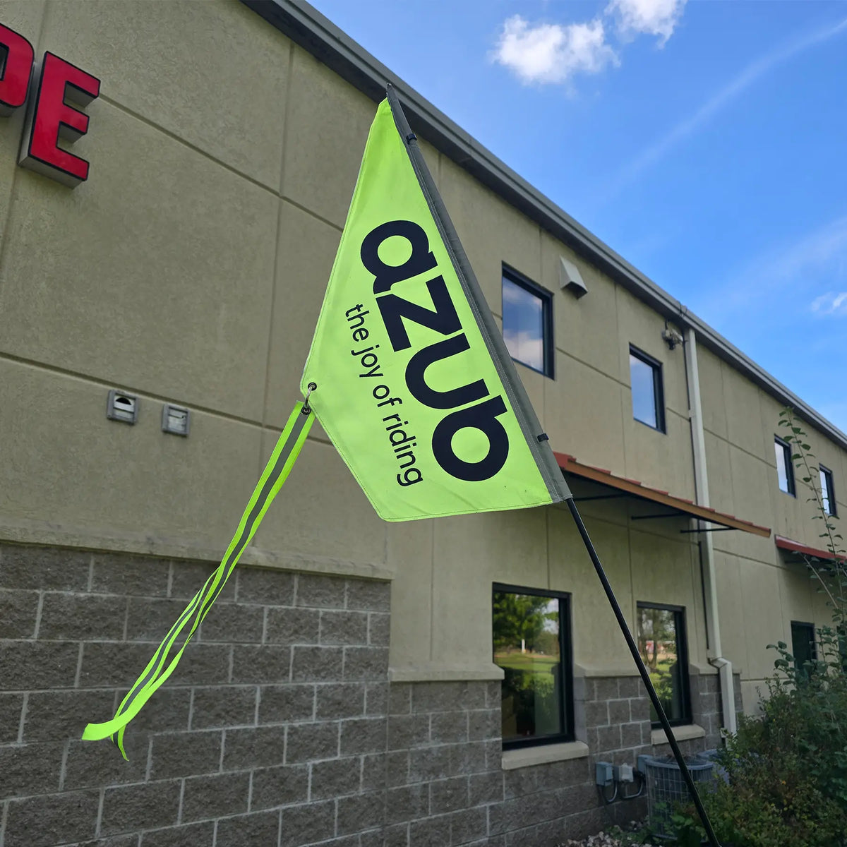 Closeup view of the Azub hi-vis yellow safety flag with a yellow tassel with a reflective stripe. The flag says "Azub - the joy of riding" in black text.