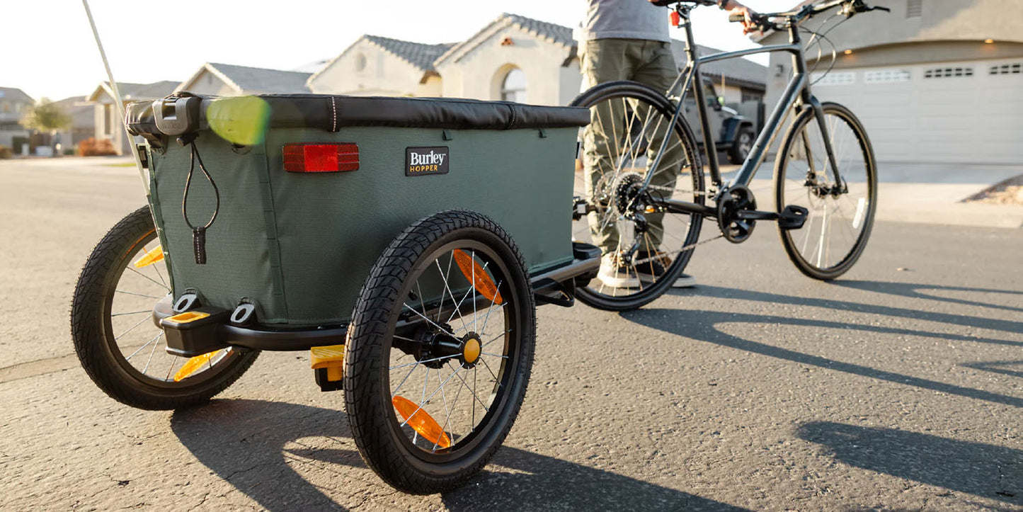 Rear quarter view of the Burley Hopper Cargo Trailer, shown attached to a bicycle on the street.