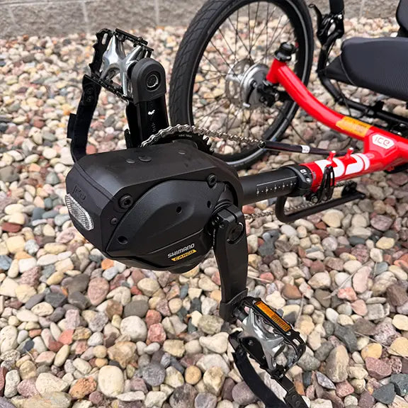Closeup view of the Shimano EP6 motor and pedals on the ICE Demo Sprint Pixel RS STEPS EP6 Passion Red Recumbent Trike in an outdoor setting.
