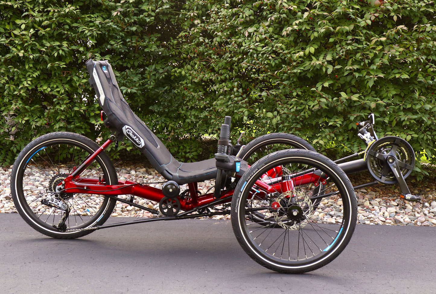 Side view of the HP Velotechnik Gekko fx 20 Sport Recumbent Trike in Magma  on a bike path against a green leafy background.