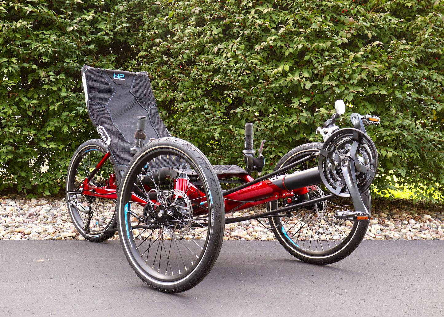 Front angled view of the HP Velotechnik Gekko fx 20 Sport Recumbent Trike in Magma on a bike path against a green leafy background.