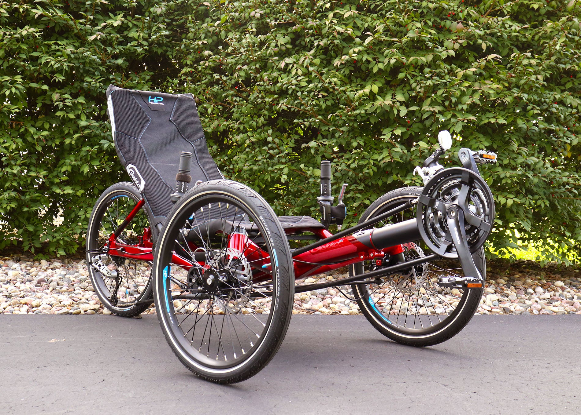 Front angled view of the HP Velotechnik Gekko fx 20 Sport Recumbent Trike in Magma on a bike path against a green leafy background.