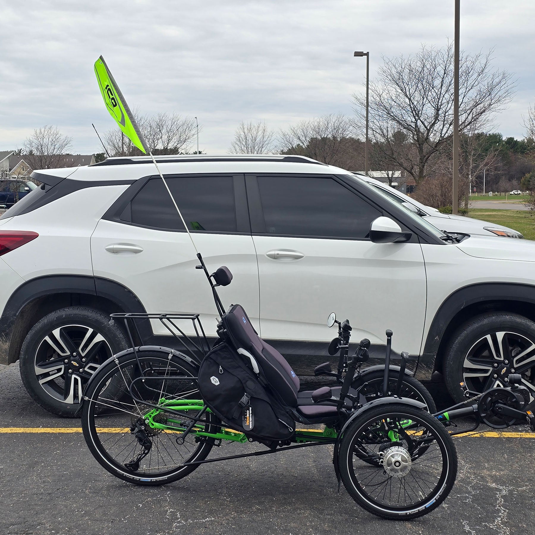 An ICE reflective safety flag mounted on an electric ICE trike on a rear light mount, sits next to a car for a height comparison. The flag is taller than the car.