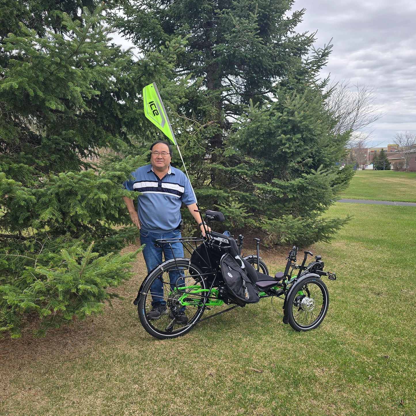 An ICE reflective safety flag mounted on an electric ICE trike on a rear light mount, sits next to a person for a height comparison. The flag is taller than the person, who is over 5 feet.