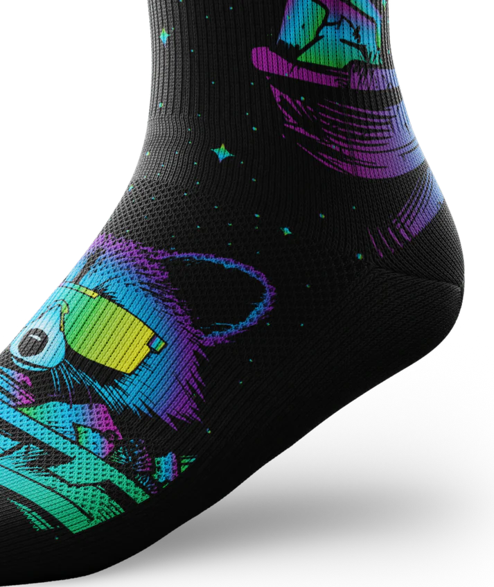 Ankle view of black socks printed with heads of racoons wearing yellow sunglasses and garbage cans.  Racoons and garbage cans are colored in blues, purples and teals.