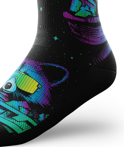Ankle view of black socks printed with heads of racoons wearing yellow sunglasses and garbage cans.  Racoons and garbage cans are colored in blues, purples and teals.