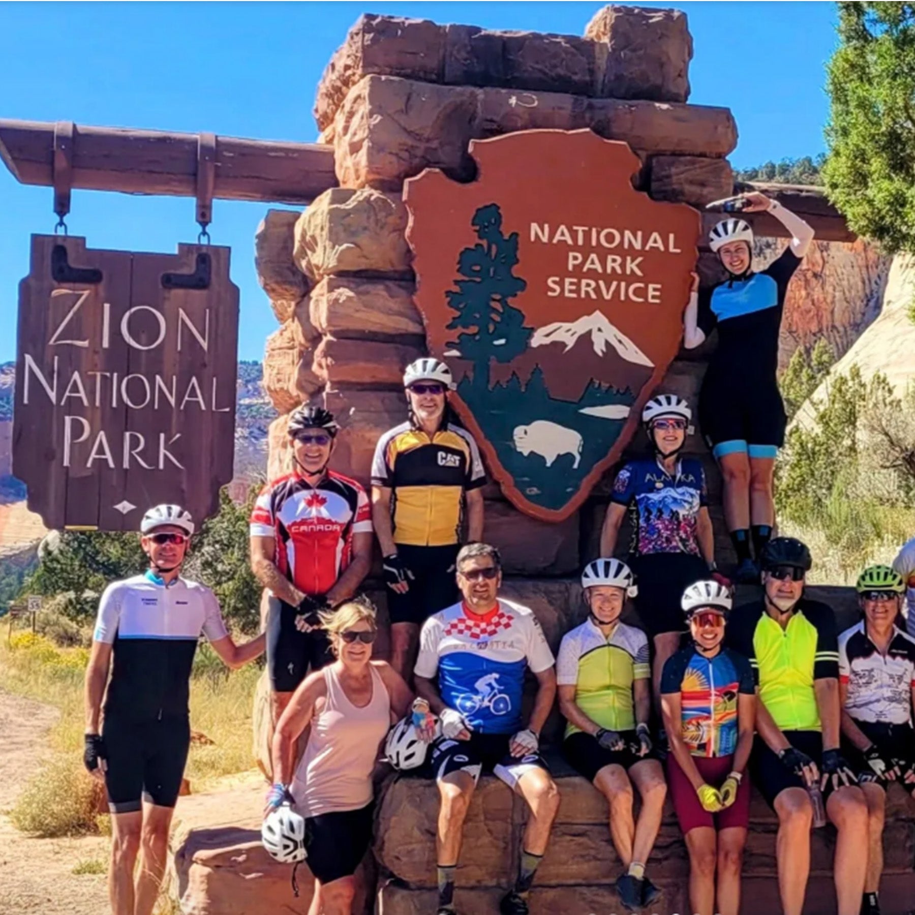 Group of cyclists posing in front of the Zion National Park sign.