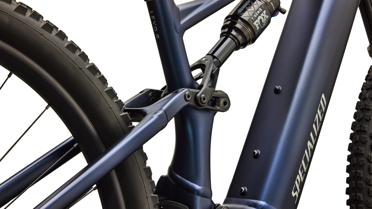 Close-up of a Specialized mountain bike frame in matte navy blue, showing the seat tube junction, rear shock, and part of the rear tire against a clean white background.