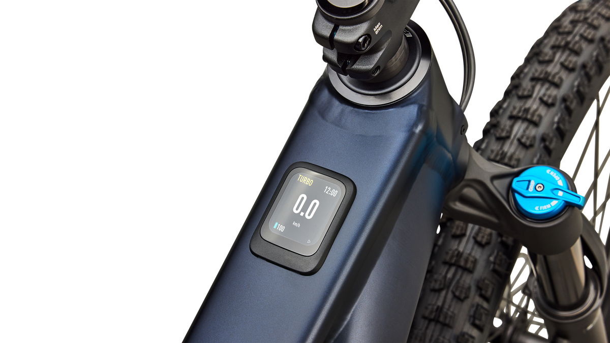 Close-up of a blue Specialized Levo R Comp Alloy electric assist mountain bike with a digital display screen, a black front fork, and part of the front tire against a white background.