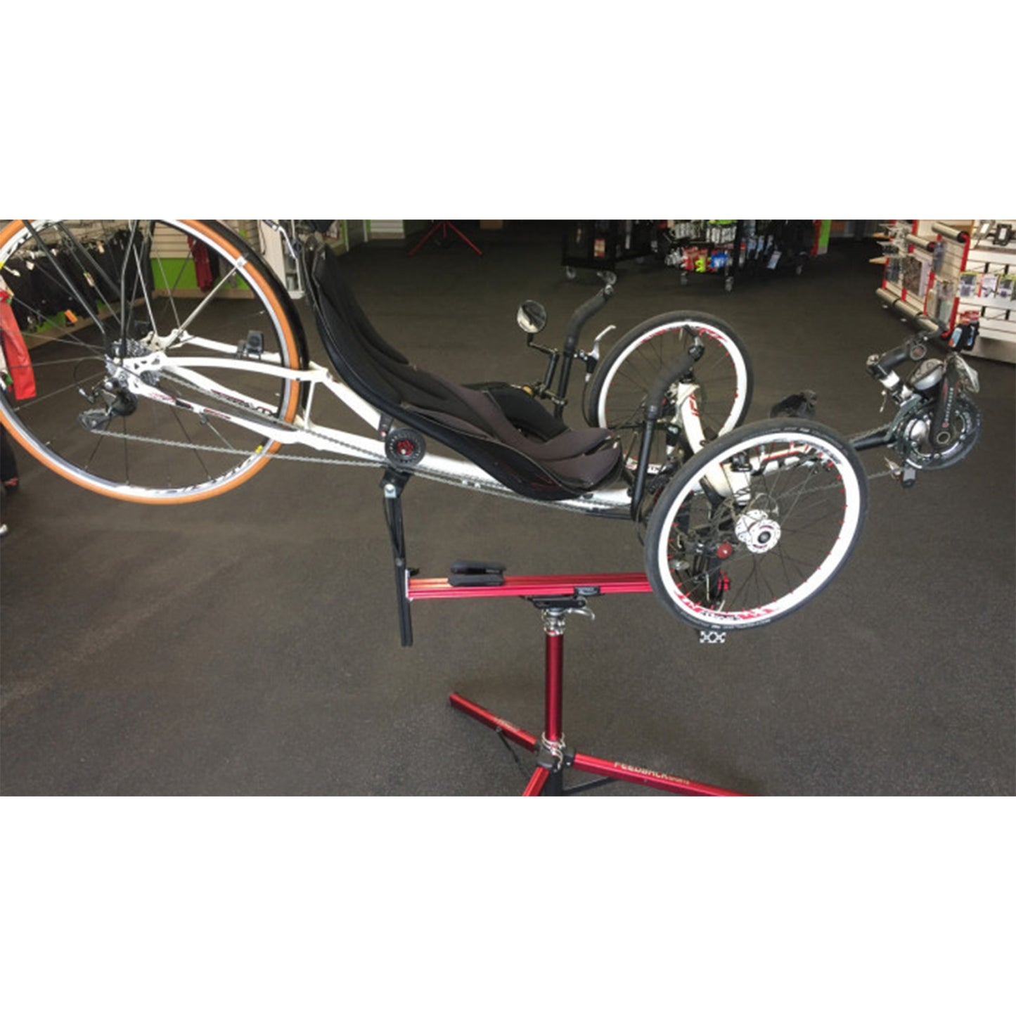 Three-wheeled recumbent trike on a red repair stand against a white background.