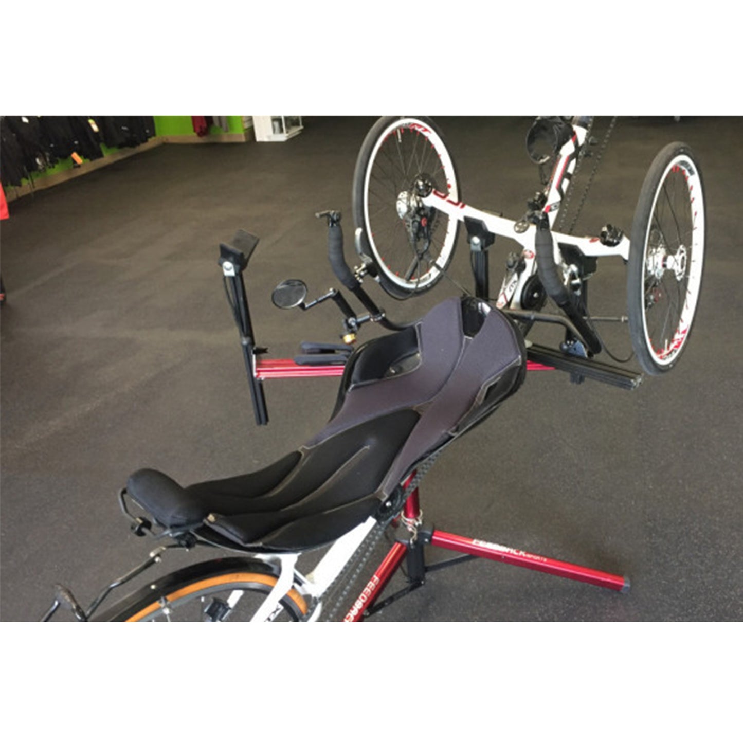 Three-wheeled recumbent trike partially on a red repair stand against a white background.