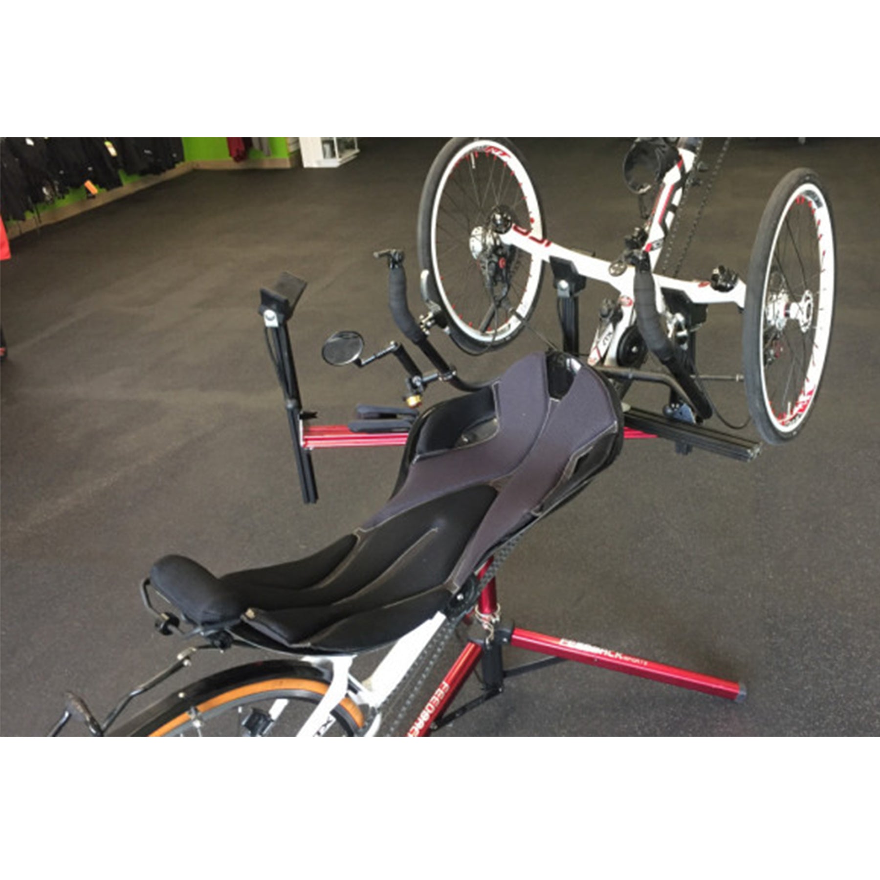 Three-wheeled recumbent trike partially on a red repair stand against a white background.