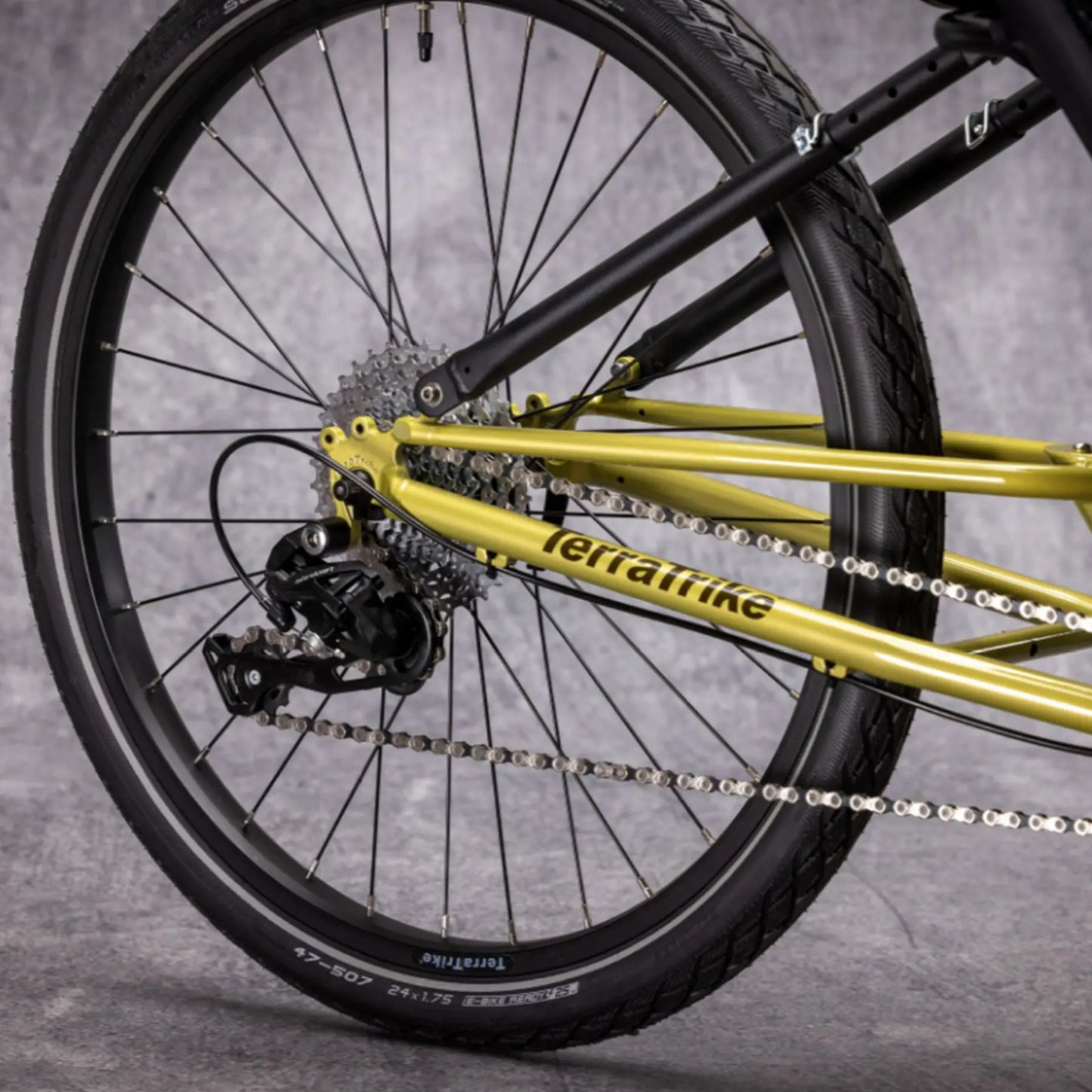 Closeup view of the rear wheel and drivetrain on the TerraTrike E.V.O. Proton Green Recumbent Trike against a gray background.
