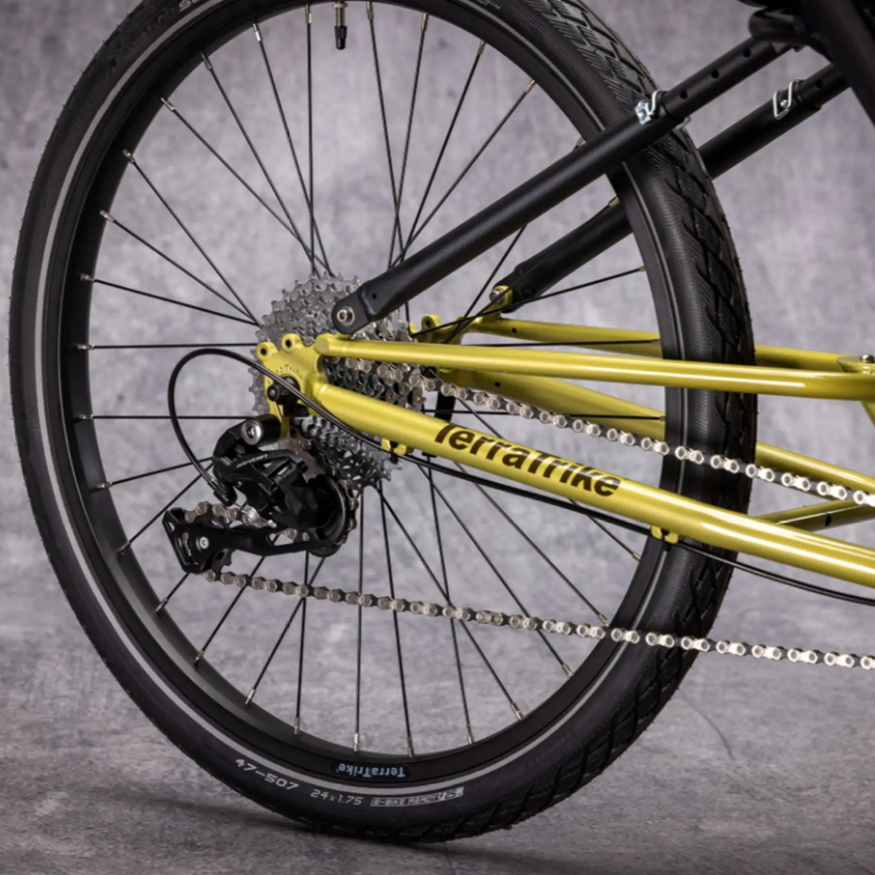 Closeup view of the rear wheel and drivetrain on the TerraTrike E.V.O. Proton Green Recumbent Trike against a gray background.
