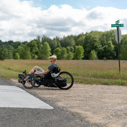A man rides a Gran Tourismo loaded with panniers on a gravel road in a country setting.