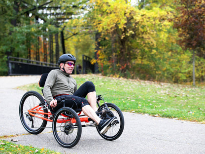 A man rides a TerraTrike GTS Recumbent Trike in Molten along a wooded bike path during fall.