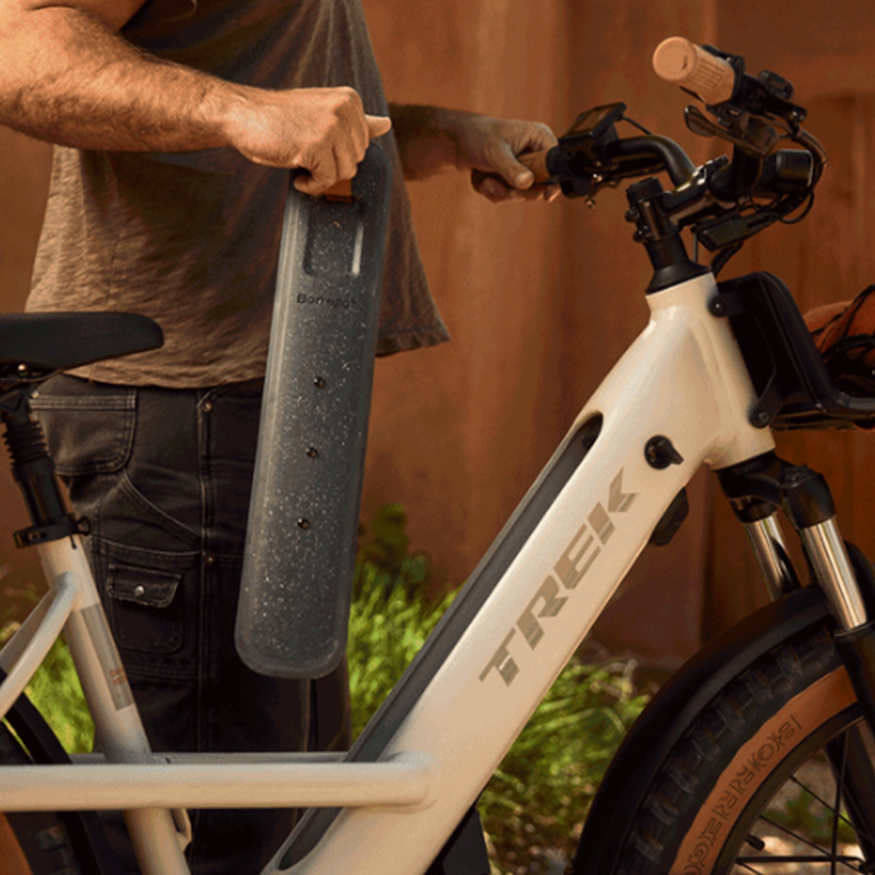 Closeup view of a man holding the battery for the Trek Borrego+ S in Matte Buff Beige in an outdoor setting.