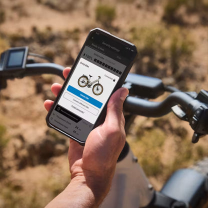 Image of a person holding a cell phone with the Trek Central App on it fo0r fine tuning control of the Trek Borrego+ S against an outdoor setting.