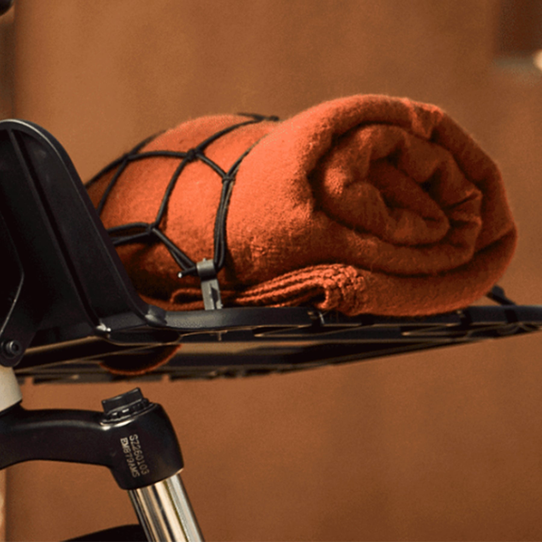 Closeup view of a rolled up blanket secured to the front rack on the Trek Borrego+ S against a blurred out outdoor background.