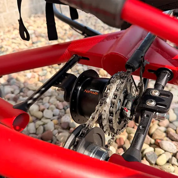 Closeup rear view of the drivetrain on the Hase Used Kettwiesel Full Suspension Red Recumbent Trike in an outdoor setting.