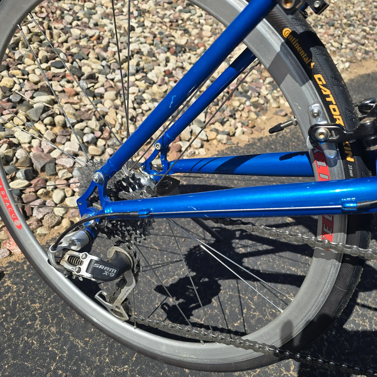 Closeup view of the wheels, tires and rear derailleur on the Used Club Dual 650c Blue Small Recumbent Bike in an outdoor setting.