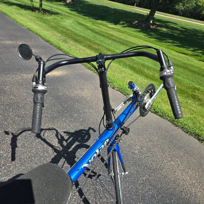 Closeup view of the handlebars and mirror on the Used Club Dual 650c Blue Small Recumbent Bike in an outdoor setting.