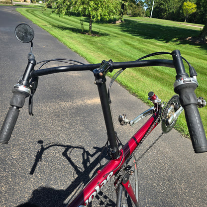 Closeup view of the handlebars and mirror on the Used Club Dual 650c Red Large Recumbent Bike in an outdoor setting.