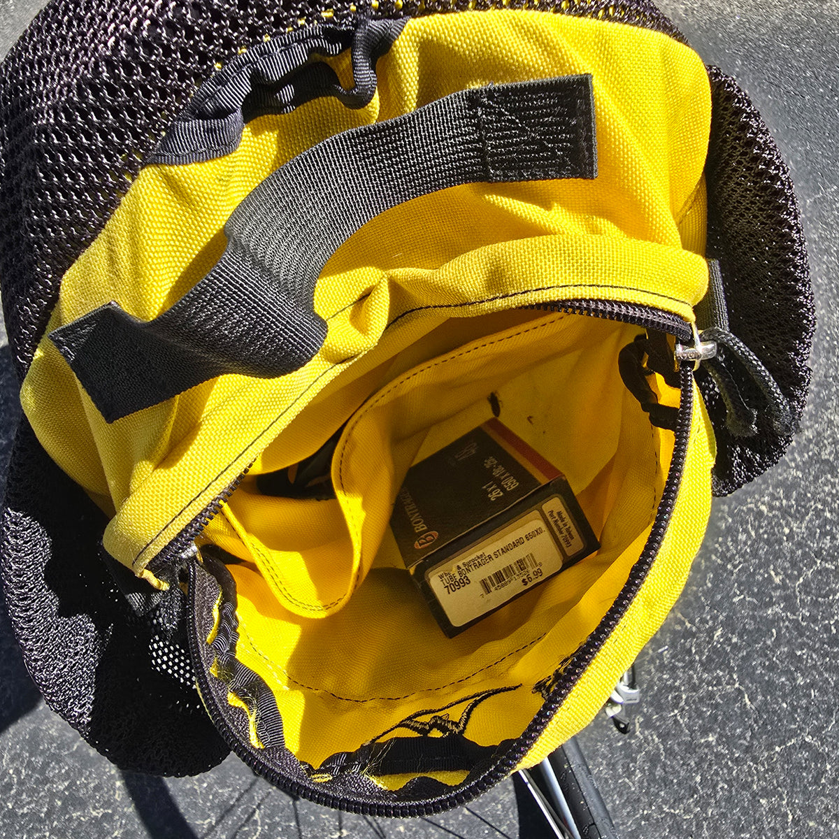 Closeup view of the inside of the yellow Hostel Shoppe seat bag, including a spare tube, on the Used Club Dual 650c Red Large Recumbent Bike in an outdoor setting.