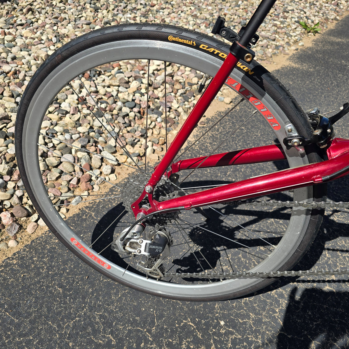 Closeup view of the wheels, tires and rear derailleur on the Used Club Dual 650c Red Large Recumbent Bike in an outdoor setting.