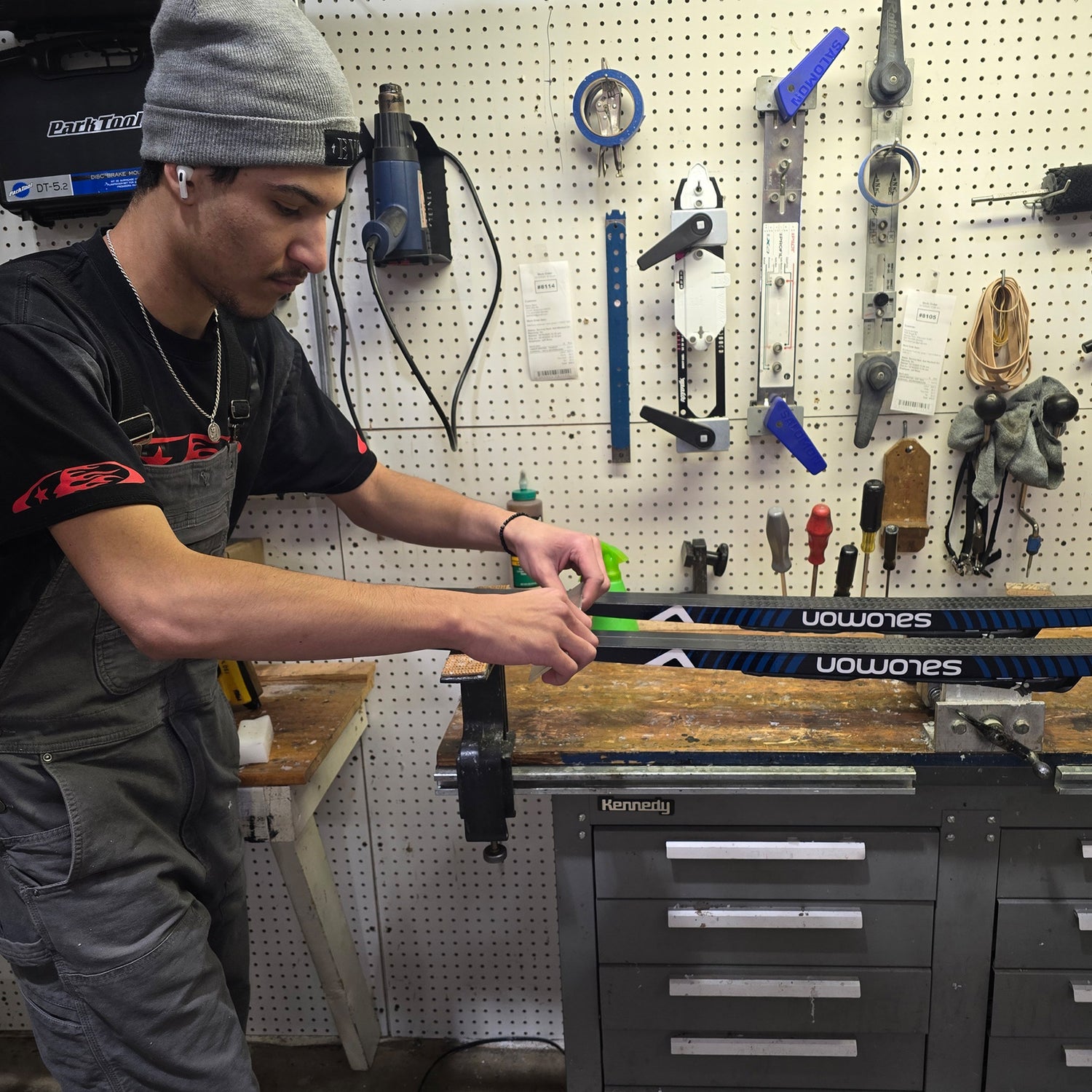 Person scraping excess wax off of a ski in a workshop.
