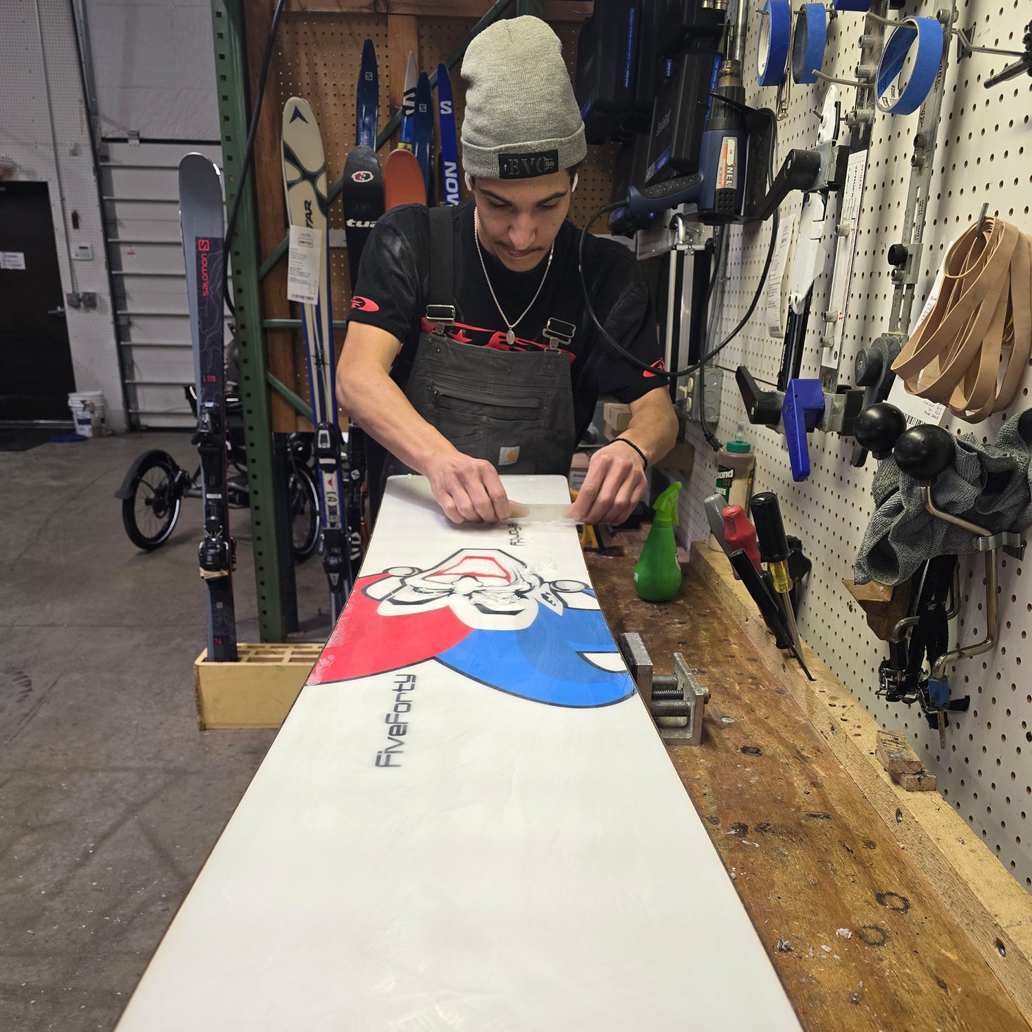 Person waxing a snowboard with a colorful design in a workshop.