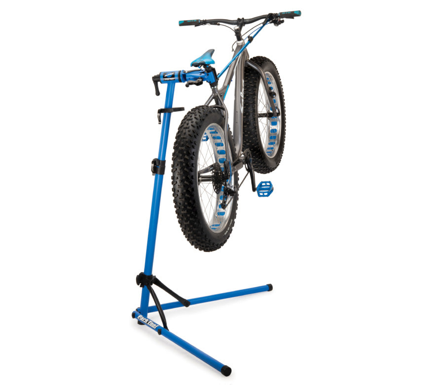 Studio image of repair stand in use with a silver fat tire bicycle mounted in the clamp.