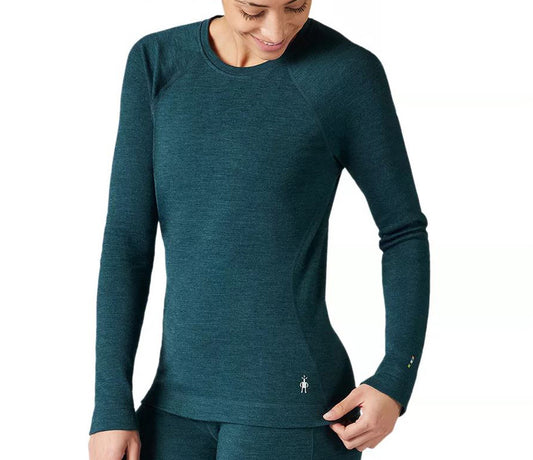 Studio image of woman wearing a Smartwool emerald green long sleeve crew neck baselayer. There is a white Smartwool logo on the bottom left of the top near the hip
