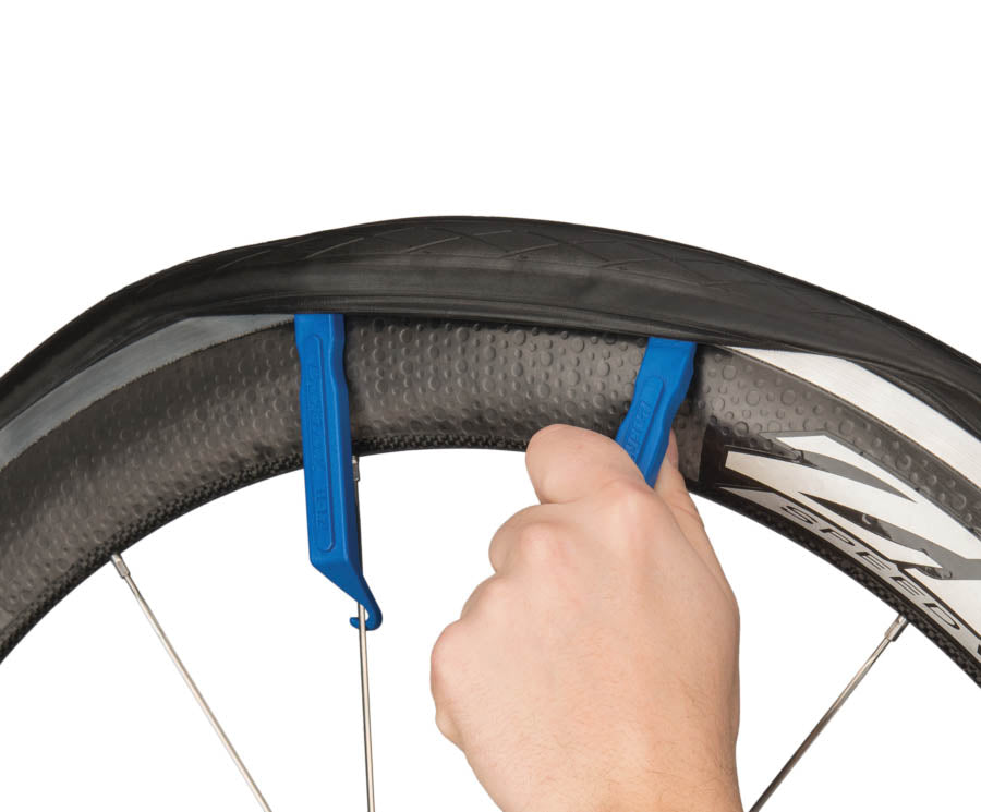 Studio image of two Park Tool blue plastic tire levers in use on a deep rim road bicycle wheel. 